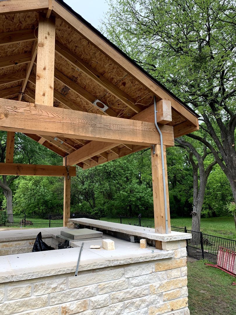 Wooden pavilion roof over a stone outdoor shelter beside a park path and trees