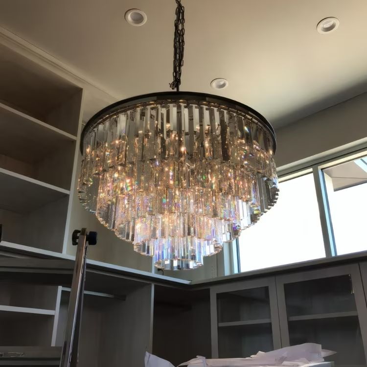 Crystal chandelier hanging in a modern room with gray built-in shelves and a window