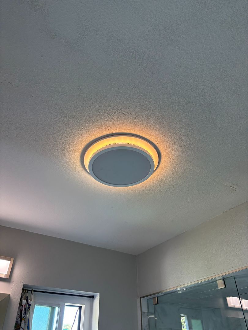 Ceiling light with warm ring glow in a bathroom, showing a mirror and shower edge below