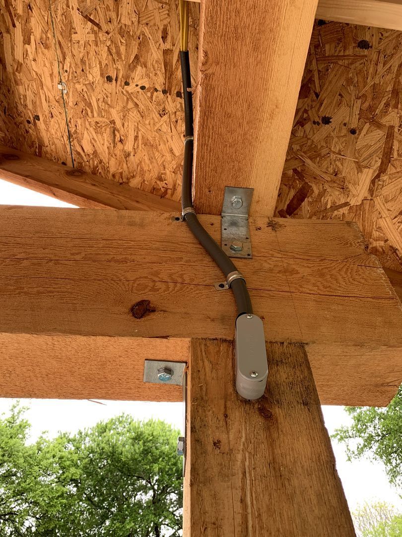 Close-up of a wooden beam ceiling with a metal conduit and junction box mounted under it