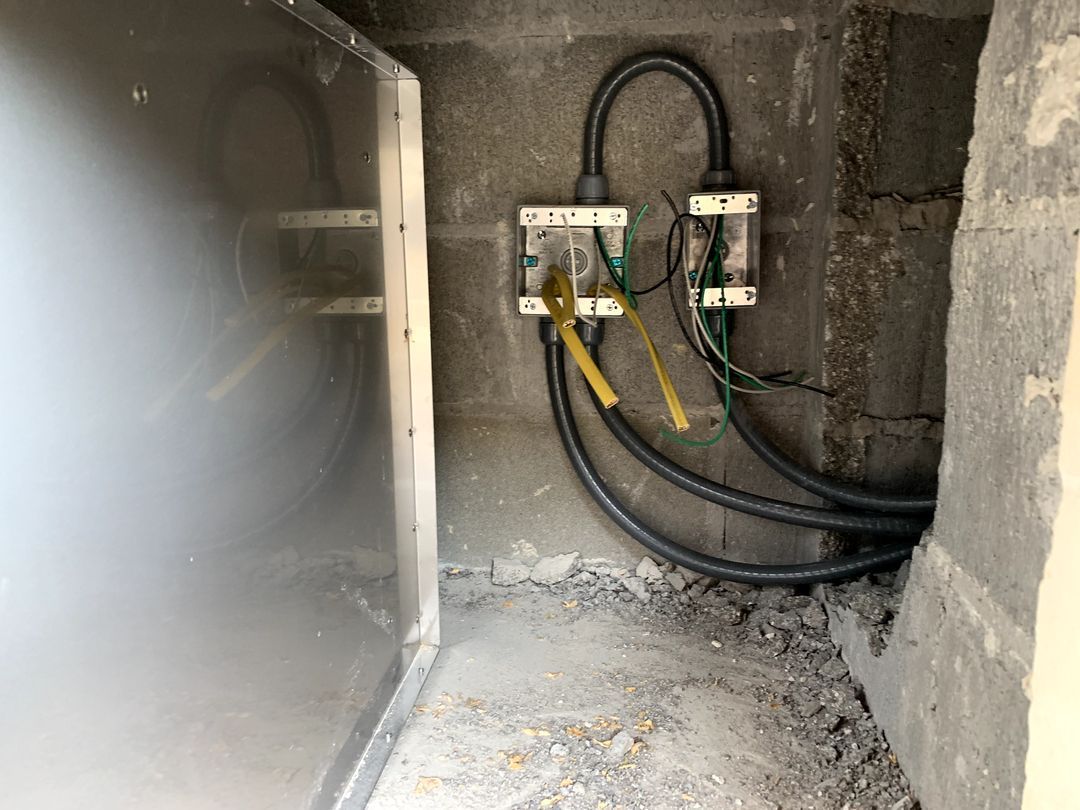 Electrical wiring and breaker boxes inside a small unfinished concrete utility room.