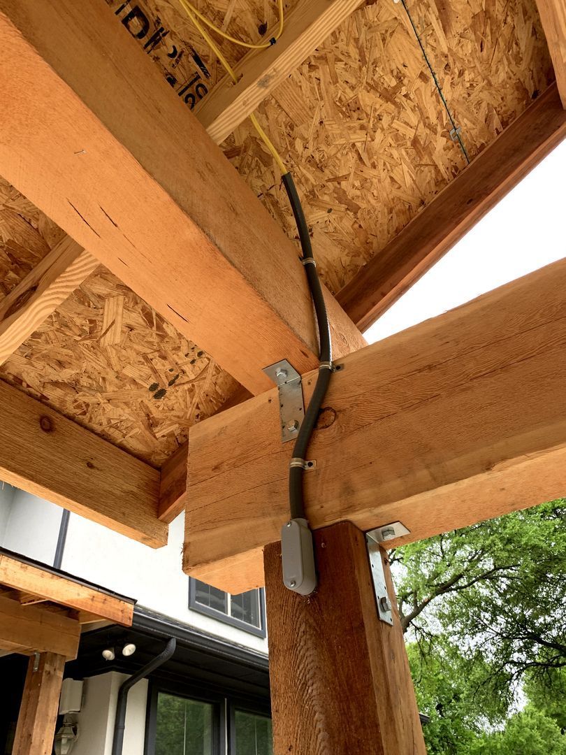 Wooden roof beam joint with a black cable and metal brackets under a porch or pergola