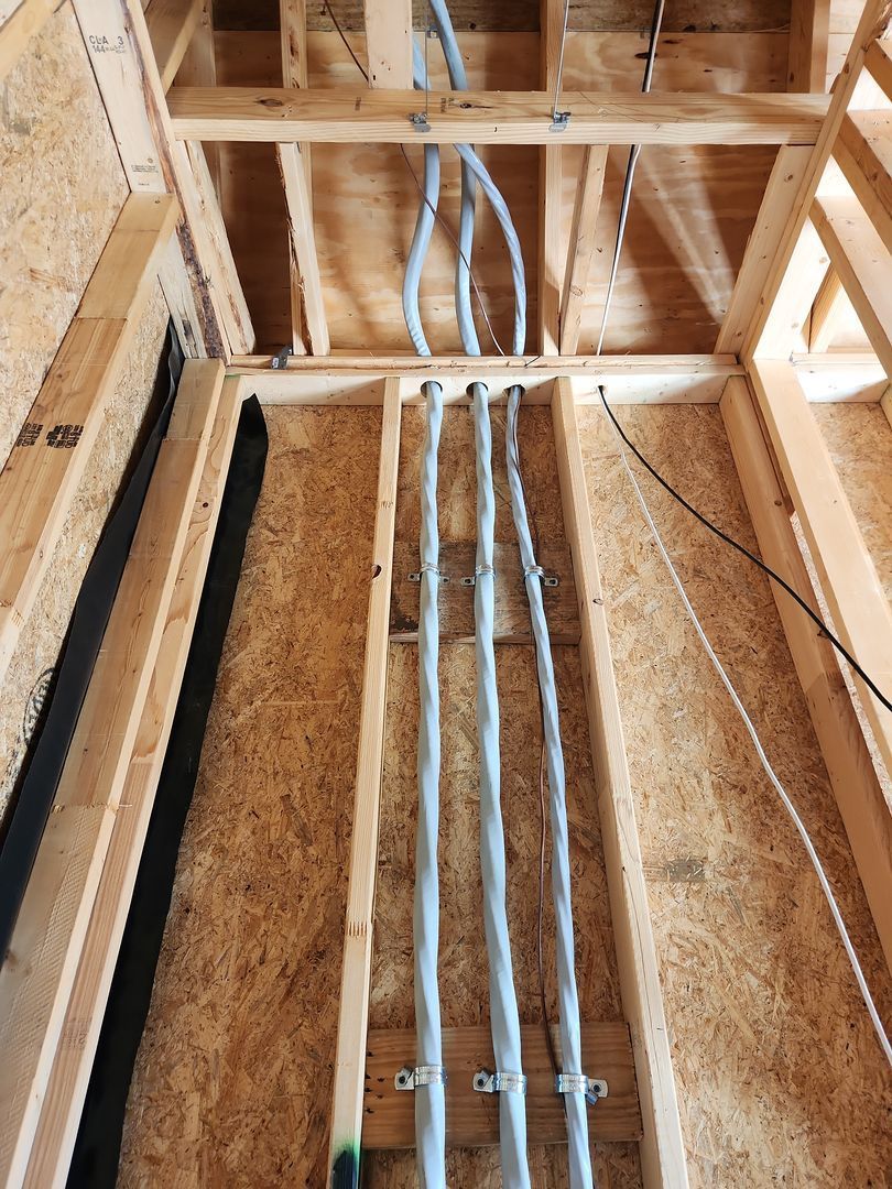 Electrical wiring running through exposed wooden wall and ceiling framing in unfinished construction.