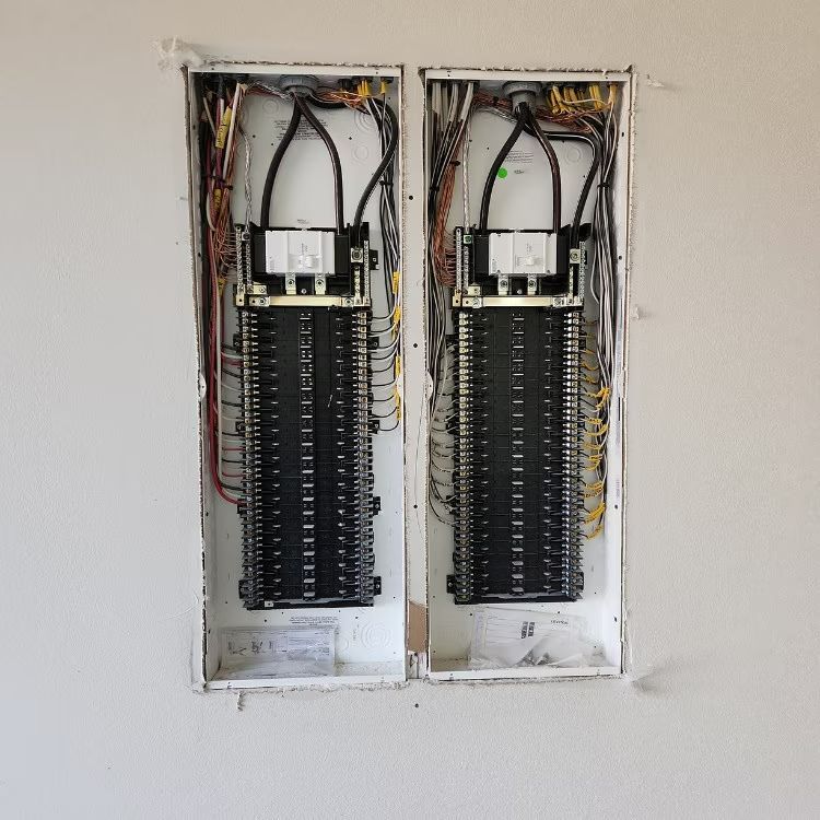 Open electrical breaker panels in a wall recess with exposed wiring