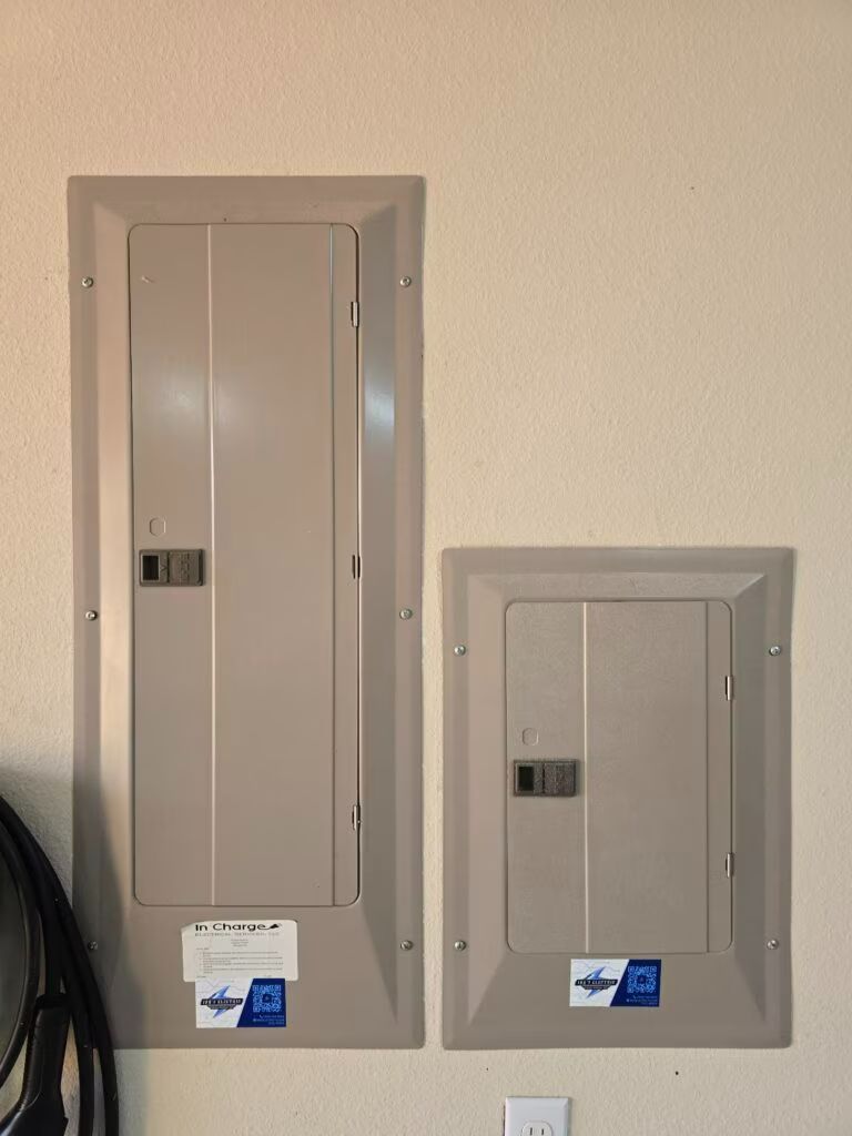 Two gray electrical breaker panels mounted on a beige wall, one large and one smaller.