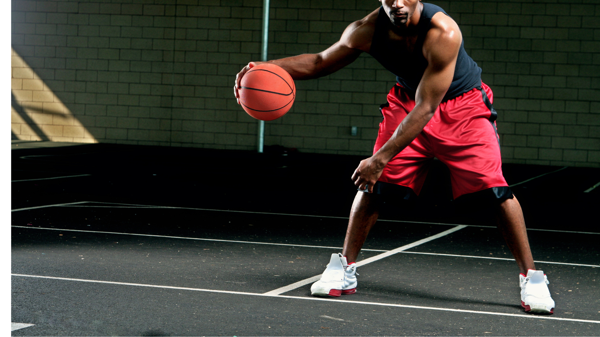 A man in red shorts is dribbling a basketball on a court