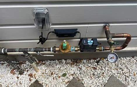 Outdoor gas pipe with valves, regulator, and pressure gauge mounted along a house wall.
