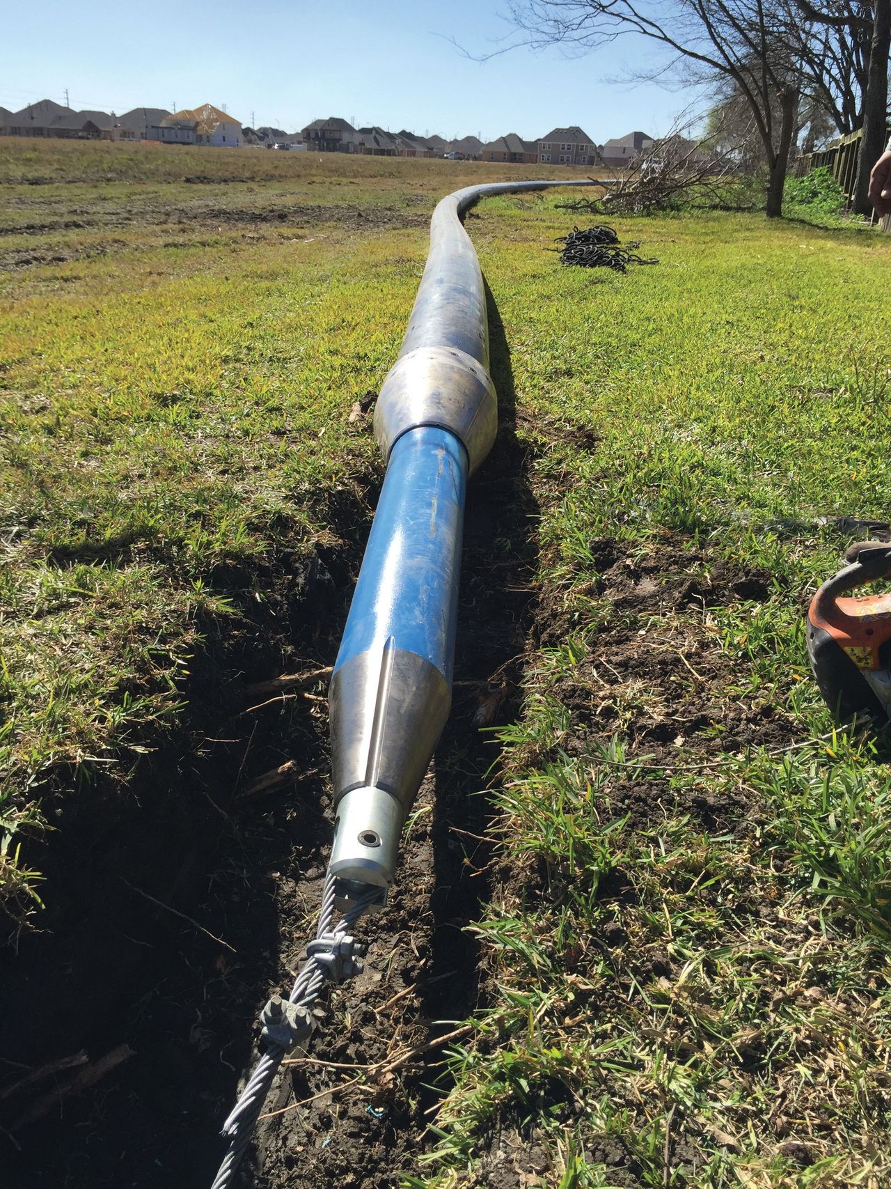Broken blue-and-white pipe lying in a grassy field under a clear sky