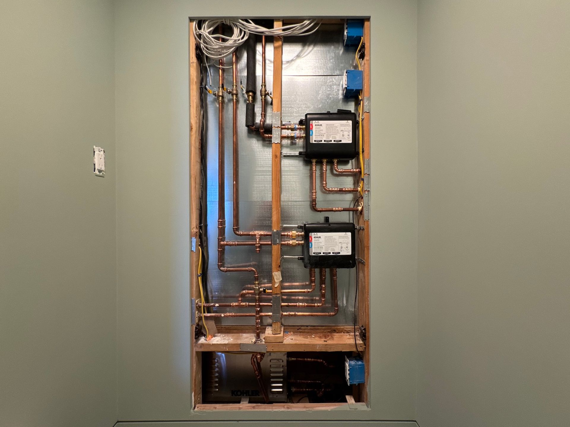 Open electrical panel with copper pipes and meters recessed in a wall.