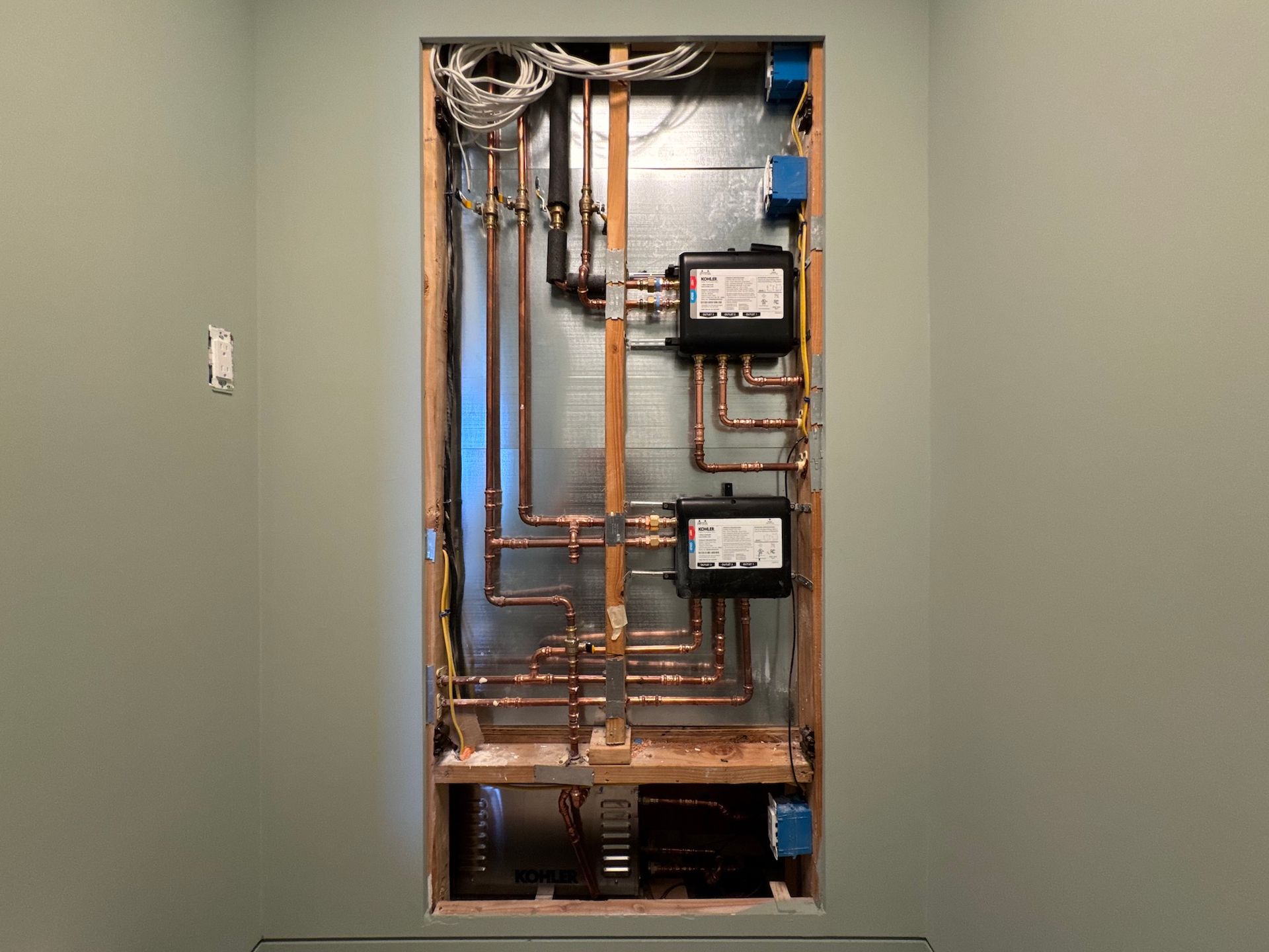 Open electrical panel with exposed copper piping and meters mounted in a wall recess