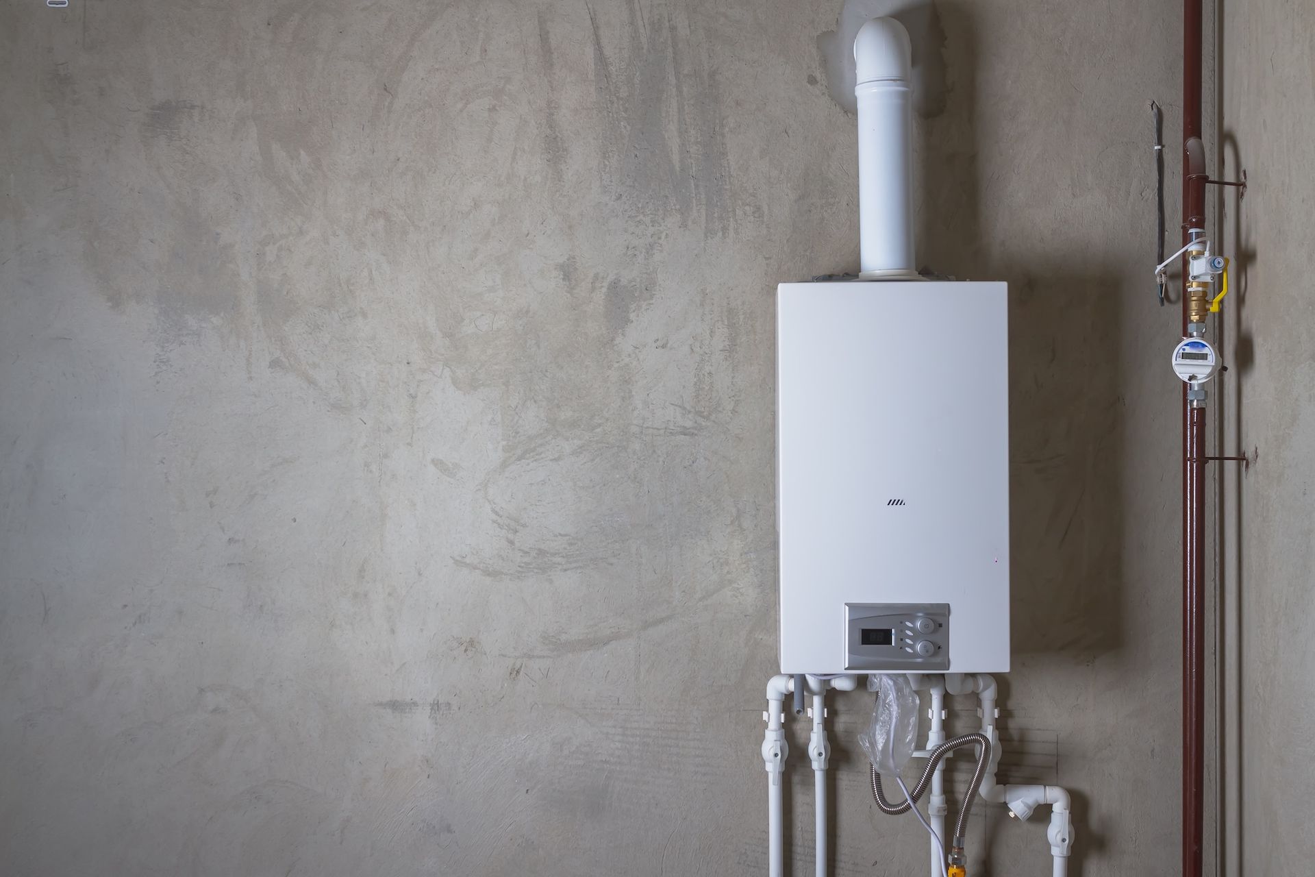 White wall-mounted boiler with pipes against an unfinished concrete wall