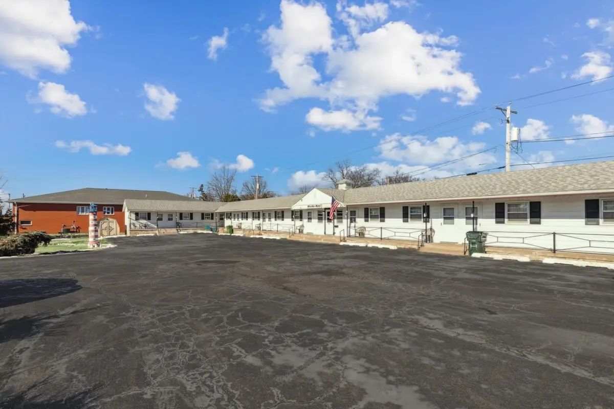 Wide paved lot beside a long white motel under a blue sky with scattered clouds