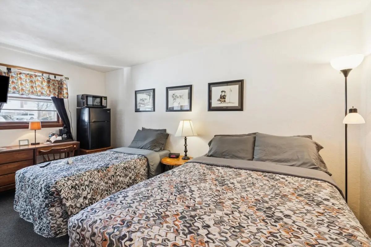 Bedroom with two beds, floral bedspreads, dresser, lamp, and framed wall art.