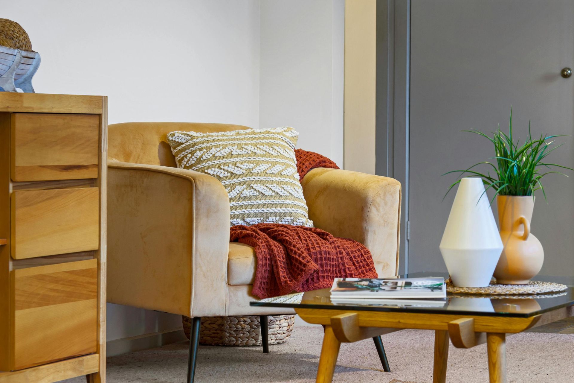 Cozy living room with tan armchair, patterned pillows, coffee table, and potted plant