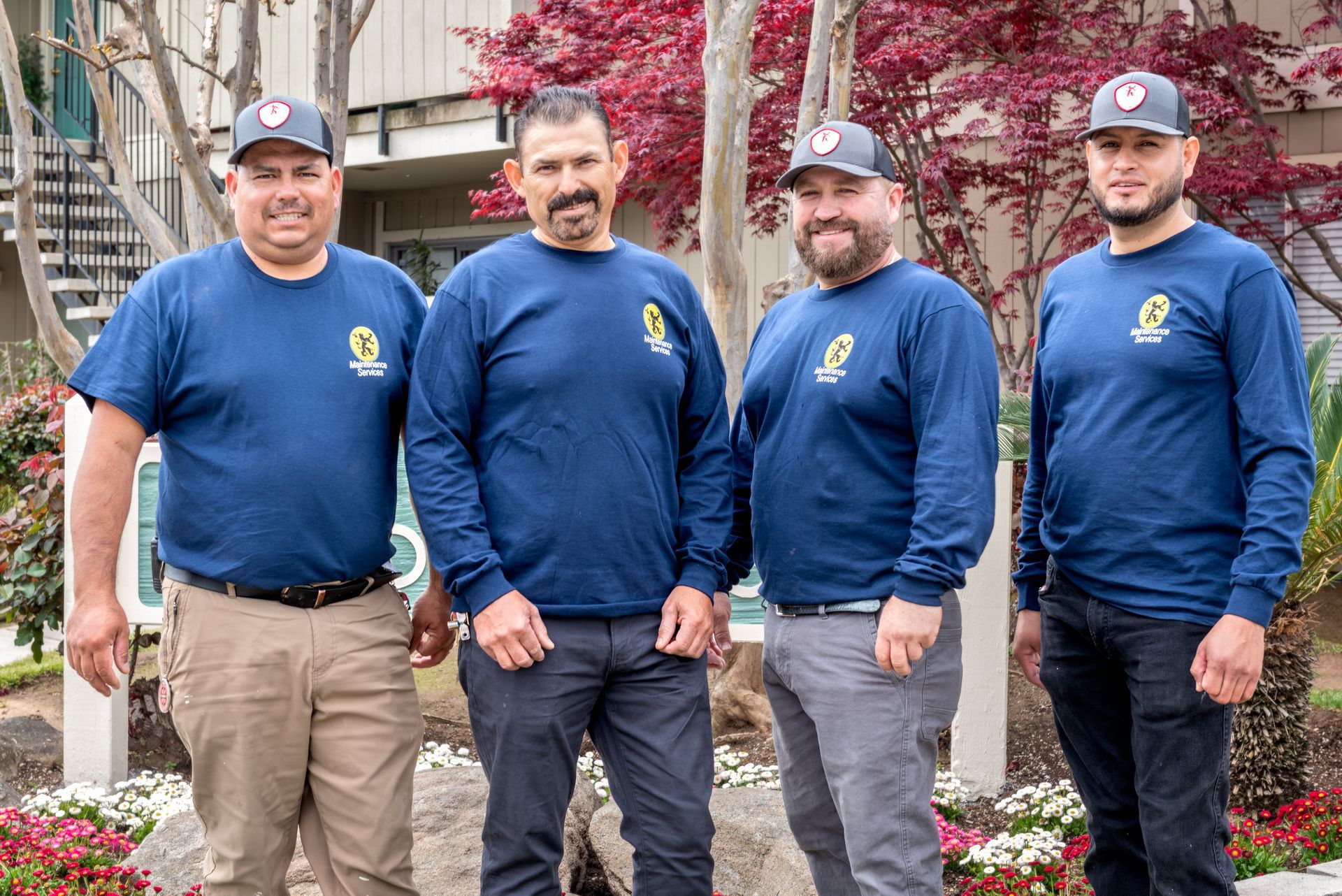 Four men in blue shirts and hats pose outside, smiling.