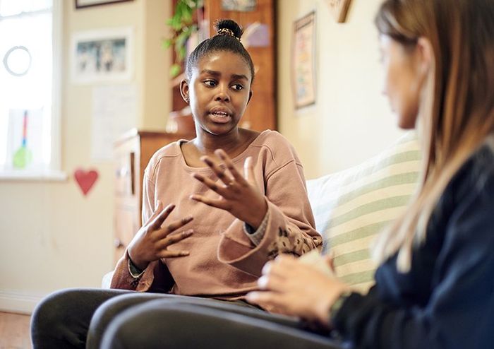 Woman gesturing while talking to another woman on a couch in a living room.