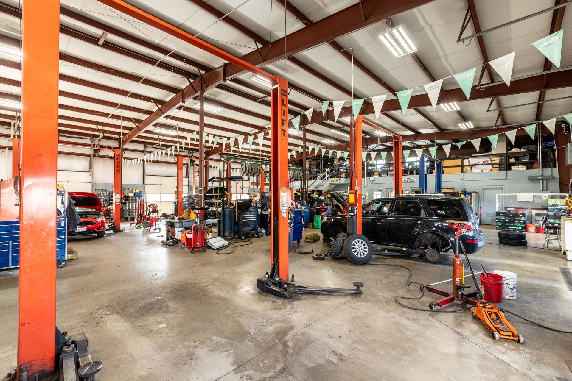 Auto repair shop with cars on lifts, red support beams, and tools across a concrete floor