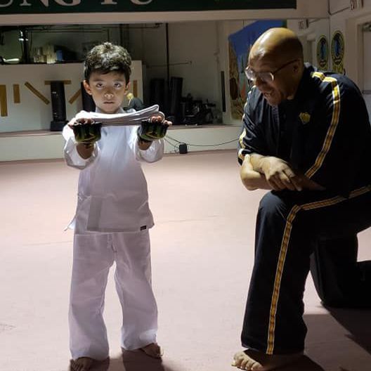 A man is kneeling down next to a young boy in a taekwondo class.