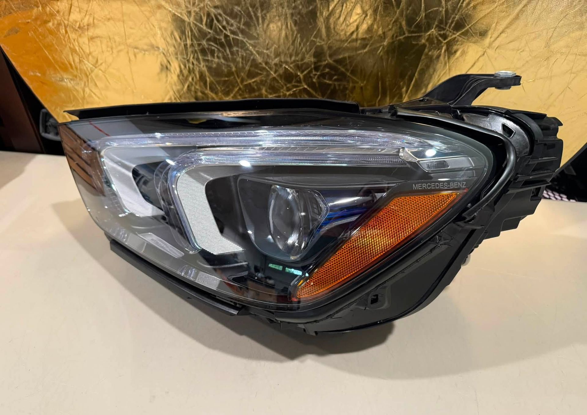 Damaged car headlight assembly with cracked black housing and clear lens on a surface