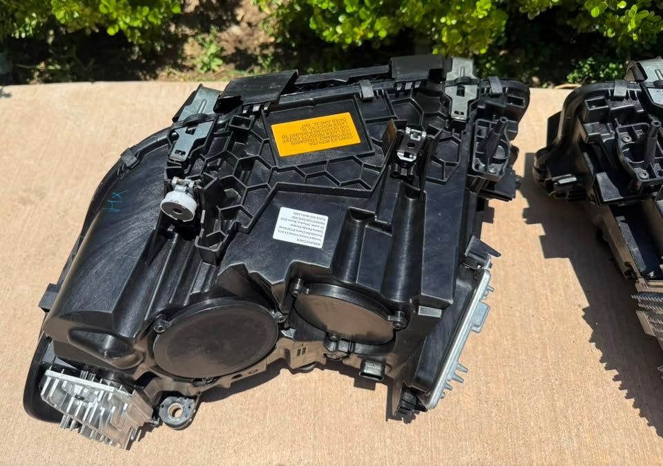 Black car part on cardboard outdoors, with a yellow label and white tag.