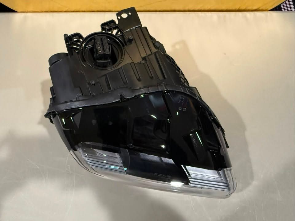Black automotive headlight assembly with clear lens and mounting bracket on a white surface