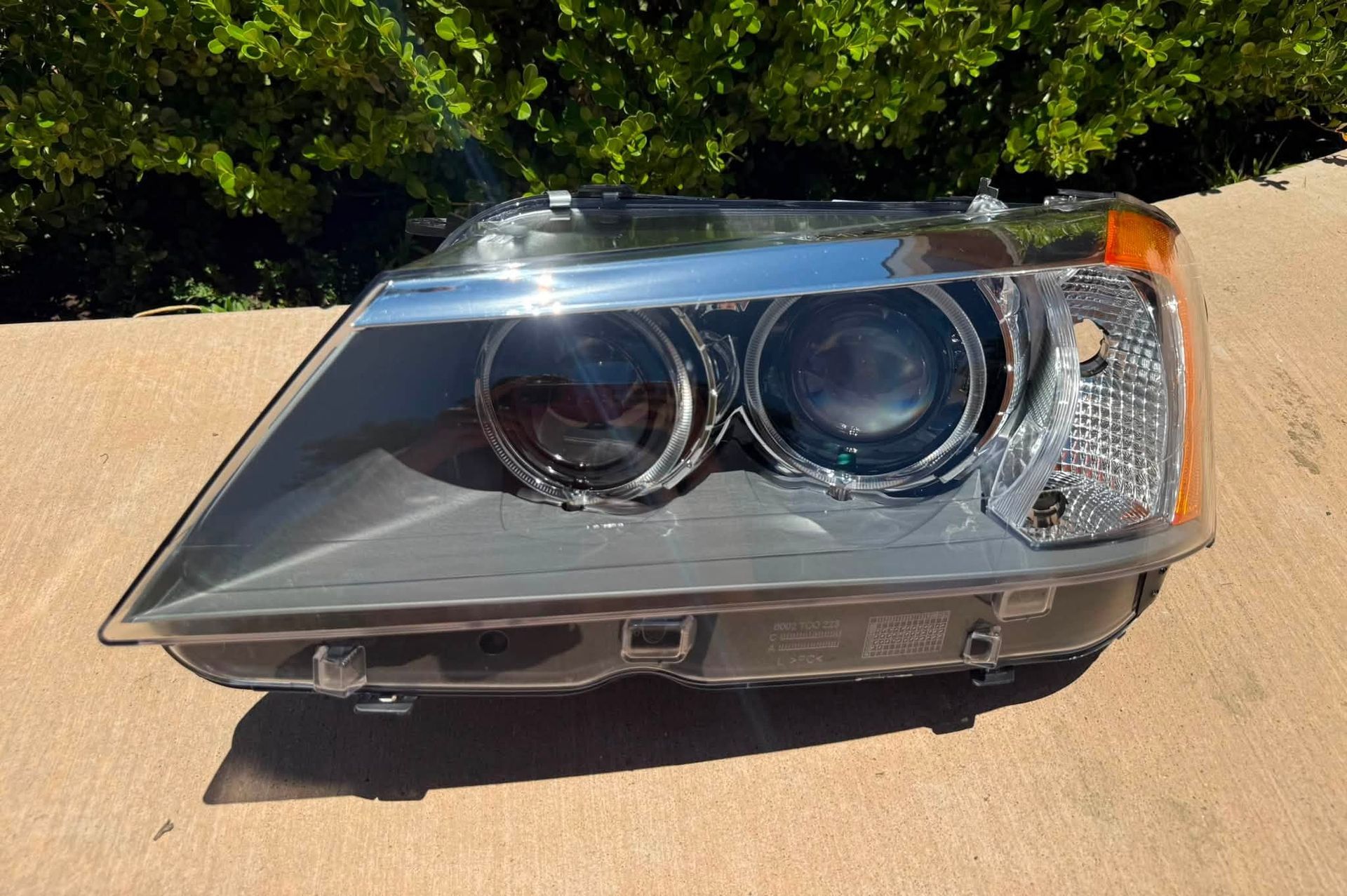 Chrome car headlight assembly resting on a concrete surface outdoors.