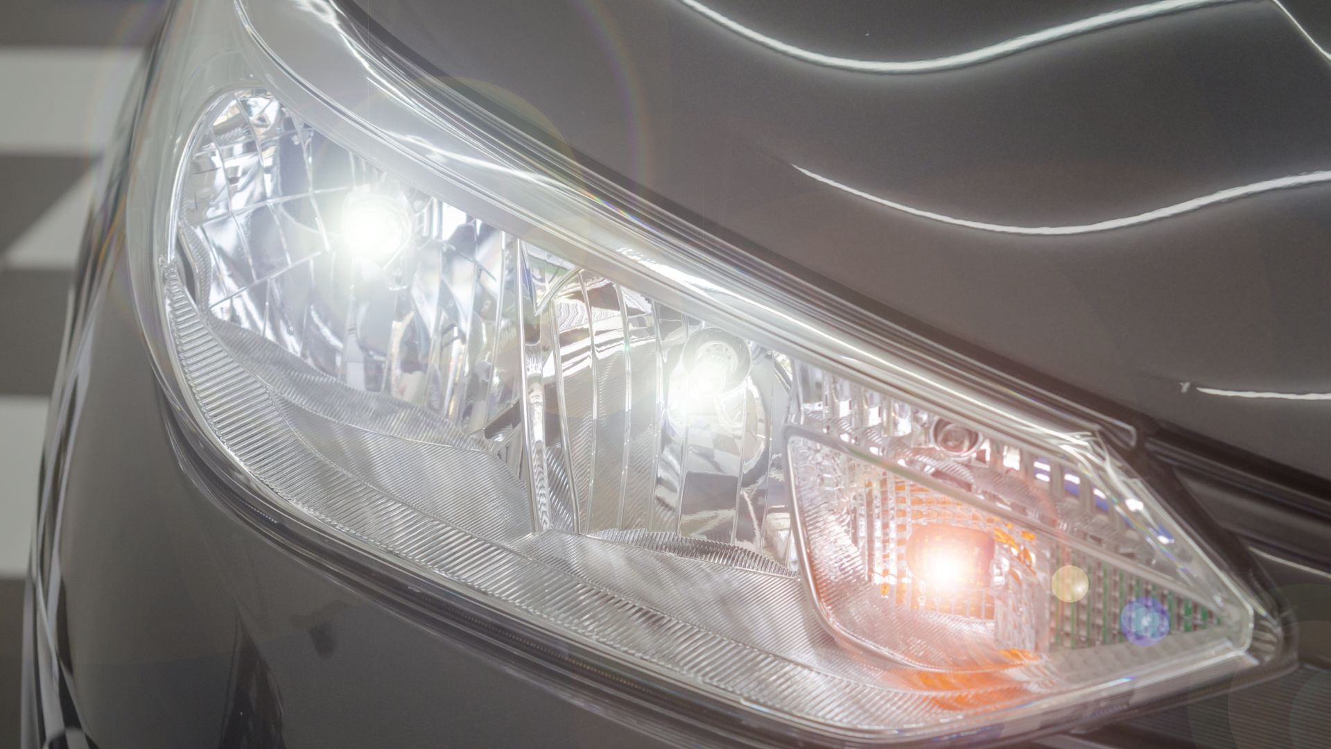 Close-up of a car headlight with silver bodywork and illuminated bulbs.