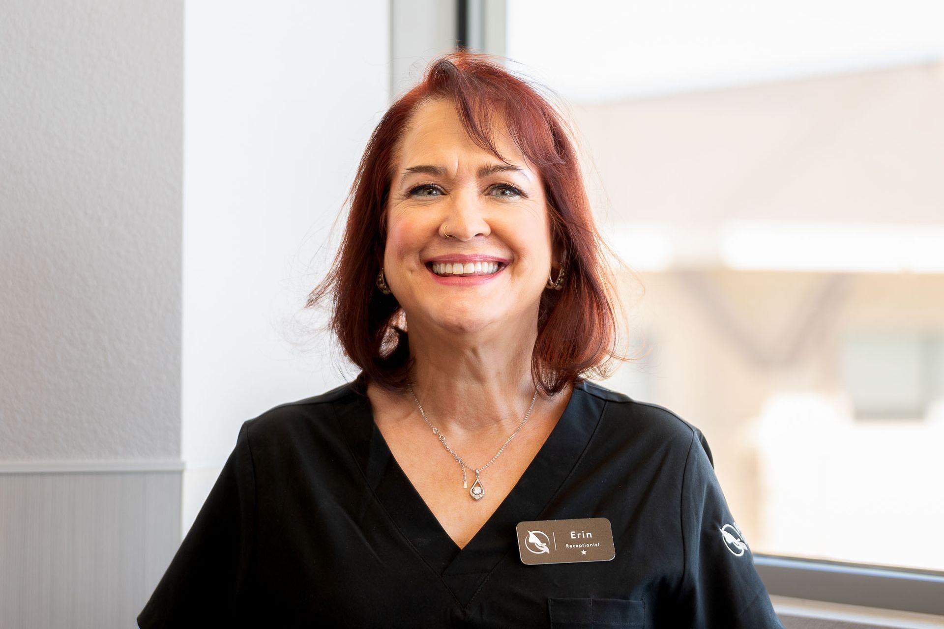 Erin who works the front desk is in a black scrub top is smiling for the camera.