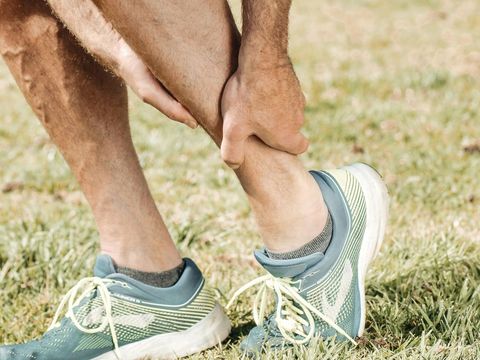 A man is holding his ankle in pain in the grass.