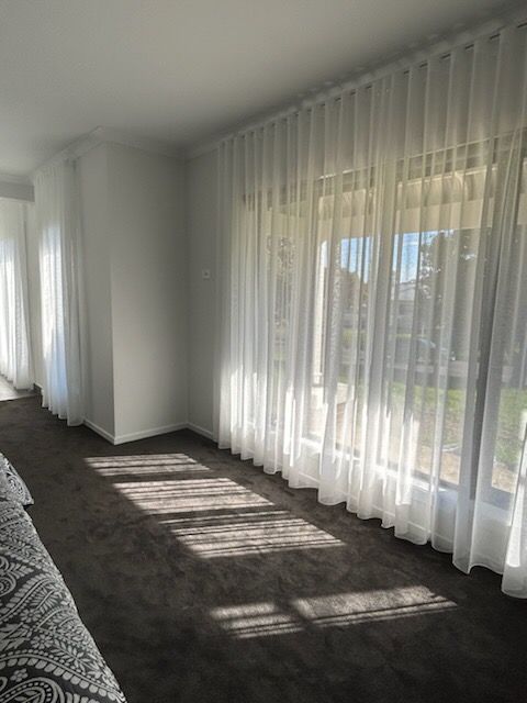 Room with sheer white curtains, sunlight casting shadows on dark carpet.