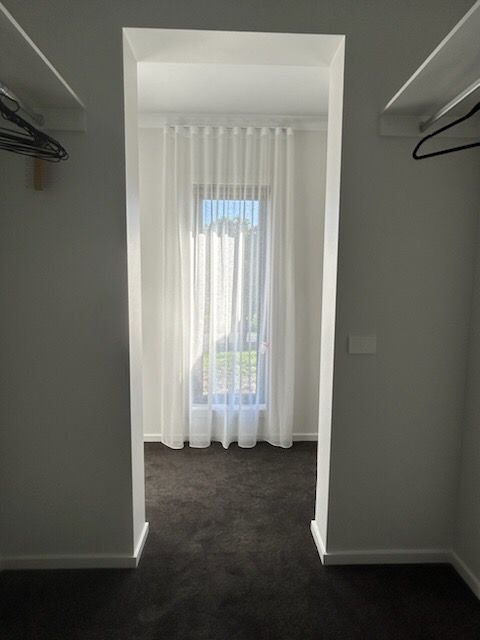 Walk-in closet leading to a room with sheer white curtains over a window. Gray walls, dark carpet.