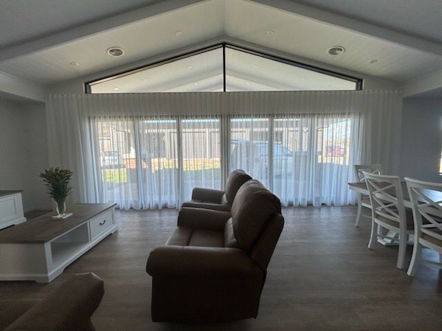 Living room with sheer white curtains on large windows, brown leather sofa, and dining area.