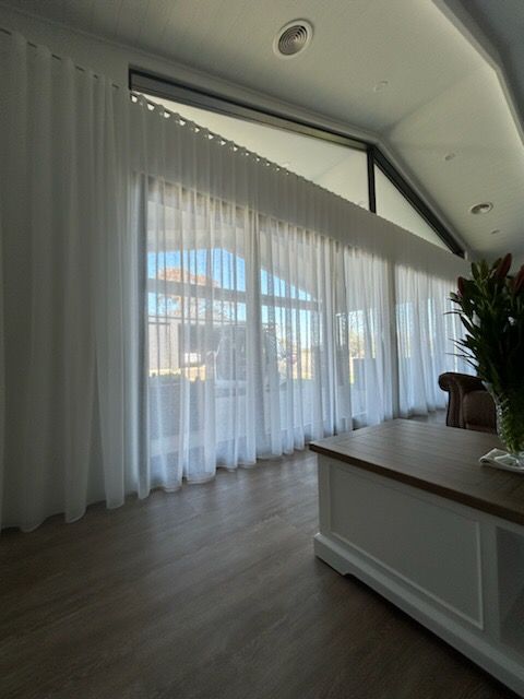 Sheer white curtains cover large windows in a bright room, hardwood floor, and an island.