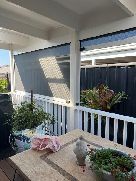 Covered outdoor patio with closed black blinds, white railing, and a table.