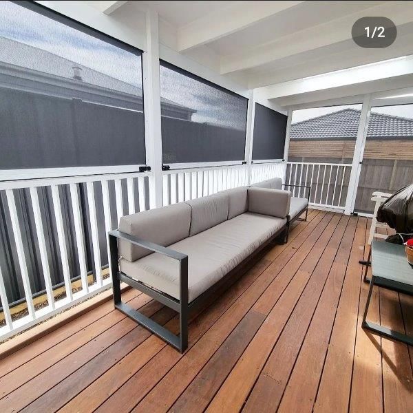Outdoor deck with gray sectional sofa, wooden floor, white railing, and black sun shades.