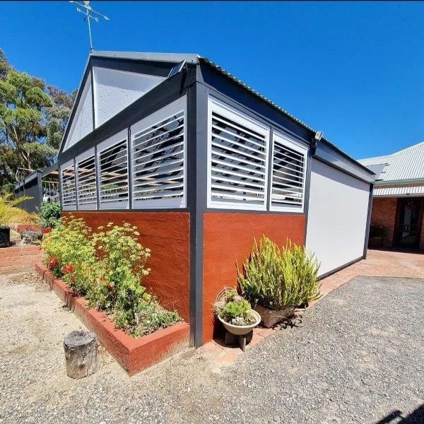 A modern building with slatted windows and a red-brown textured wall, surrounded by plants and gravel.