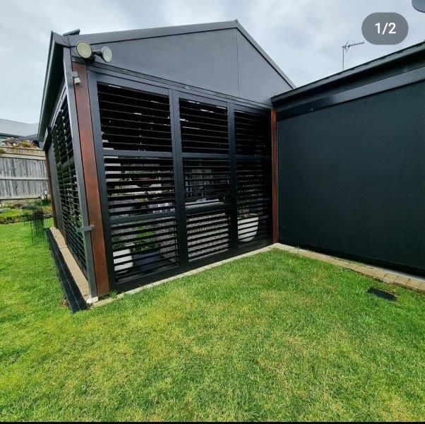 Black louvered outdoor shutters on a dark-roofed structure, brown trim, green lawn.
