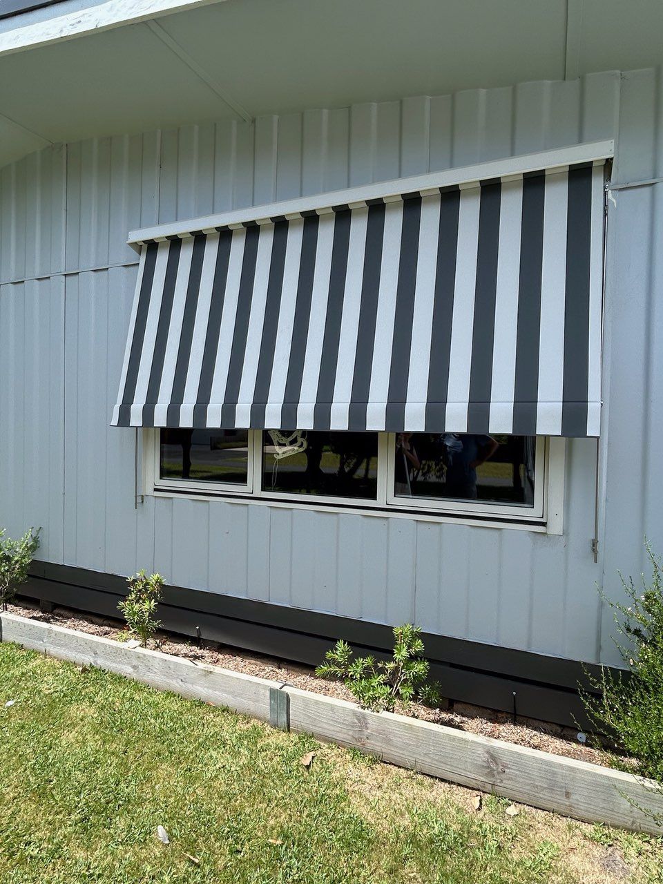 Gray and white striped awning over a window on a light blue house.