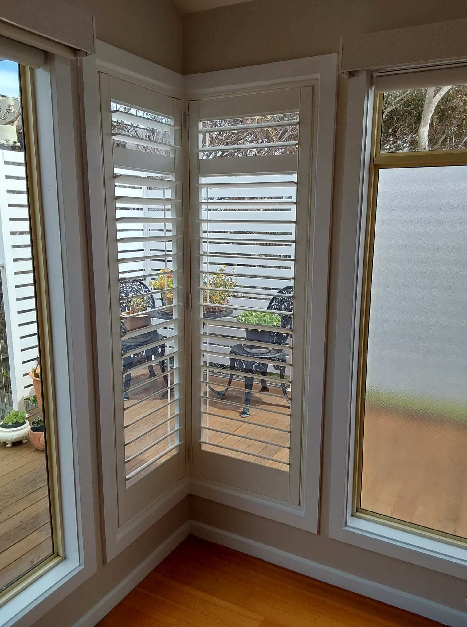 Corner room with white shuttered windows, overlooking a deck.
