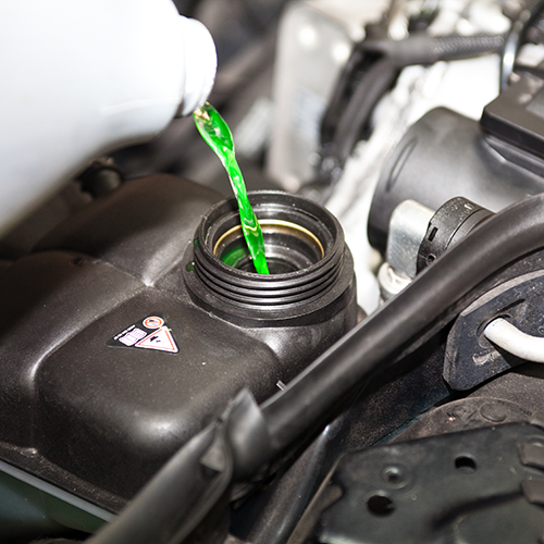 Green coolant being poured into a car engine reservoir under the hood.