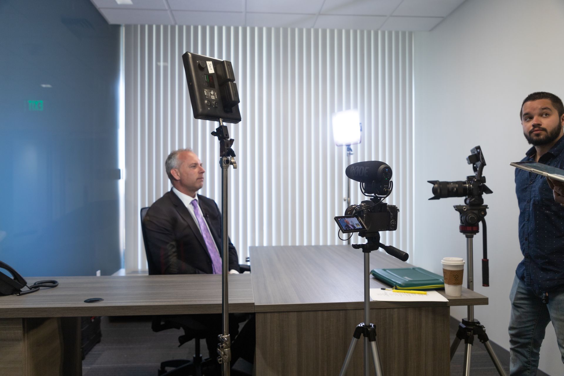 A man in a suit and tie is sitting at a desk in front of a camera.