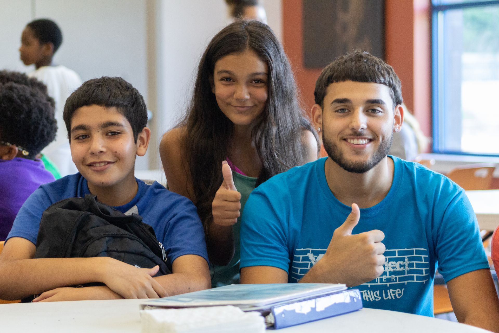 A group of young people are sitting at a table giving a thumbs up.