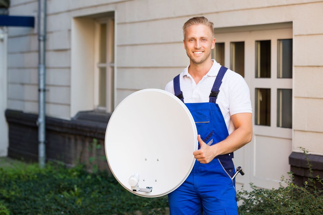 Man in blue overalls holding a satellite dish, smiling in front of a building. Man in blue overalls holding a satellite dish, smiling in front of a building.