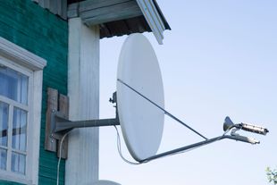 White satellite dish attached to the green wooden side of a house. White satellite dish attached to the green wooden side of a house.