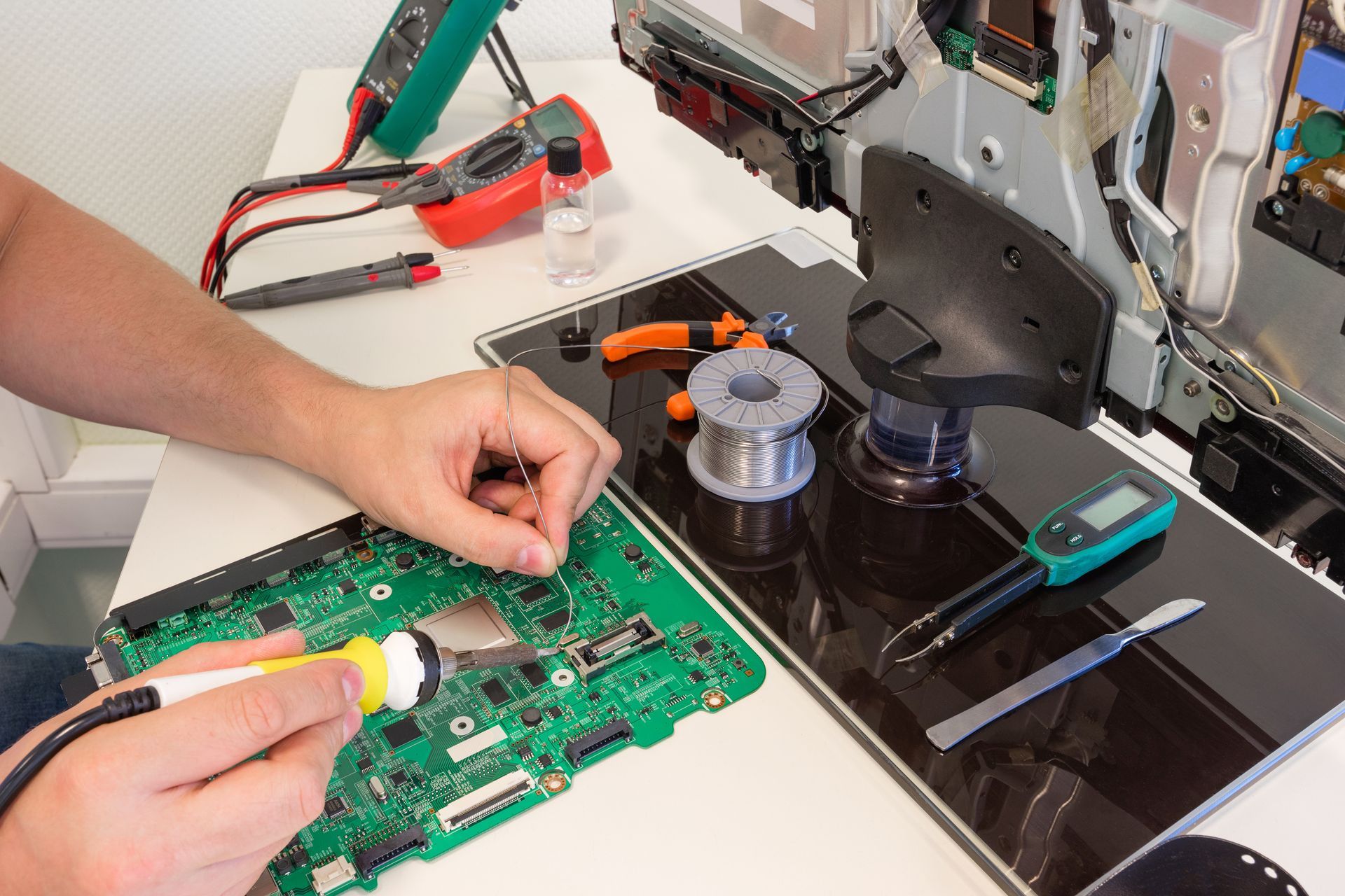 Person soldering circuit board, working on TV components with tools like multimeters and tweezers on a white table. Person soldering circuit board, working on TV components with tools like multimeters and tweezers on a white table.