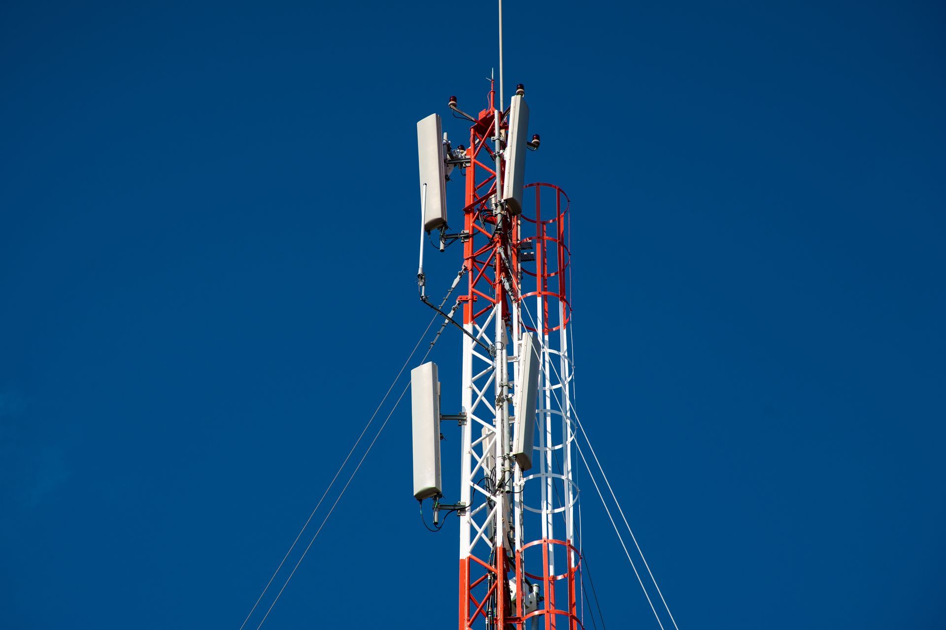 Red and white cell tower against a clear blue sky, with antennas.