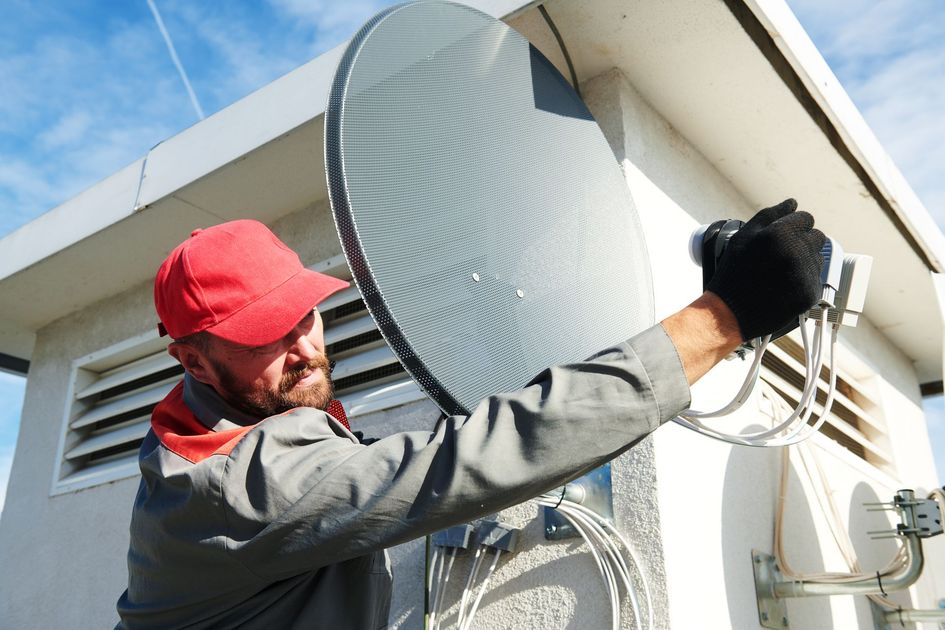 Man in red cap installs a satellite dish on a building exterior. Man in red cap installs a satellite dish on a building exterior.