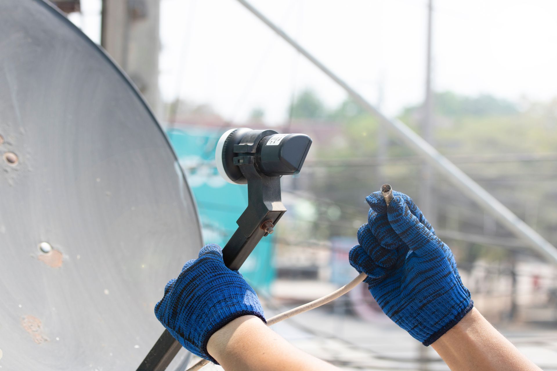 Person in blue gloves connecting a coaxial cable to a satellite dish.