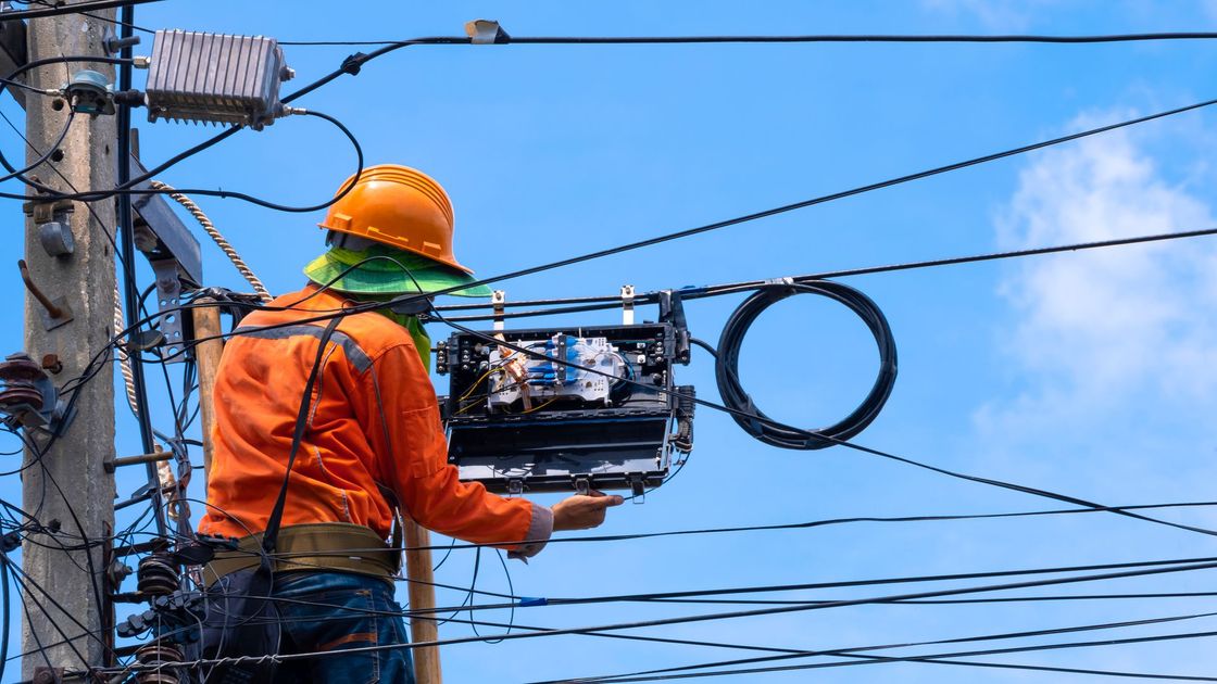 Lineman in orange suit working on utility pole with wires and cables against blue sky. Lineman in orange suit working on utility pole with wires and cables against blue sky.