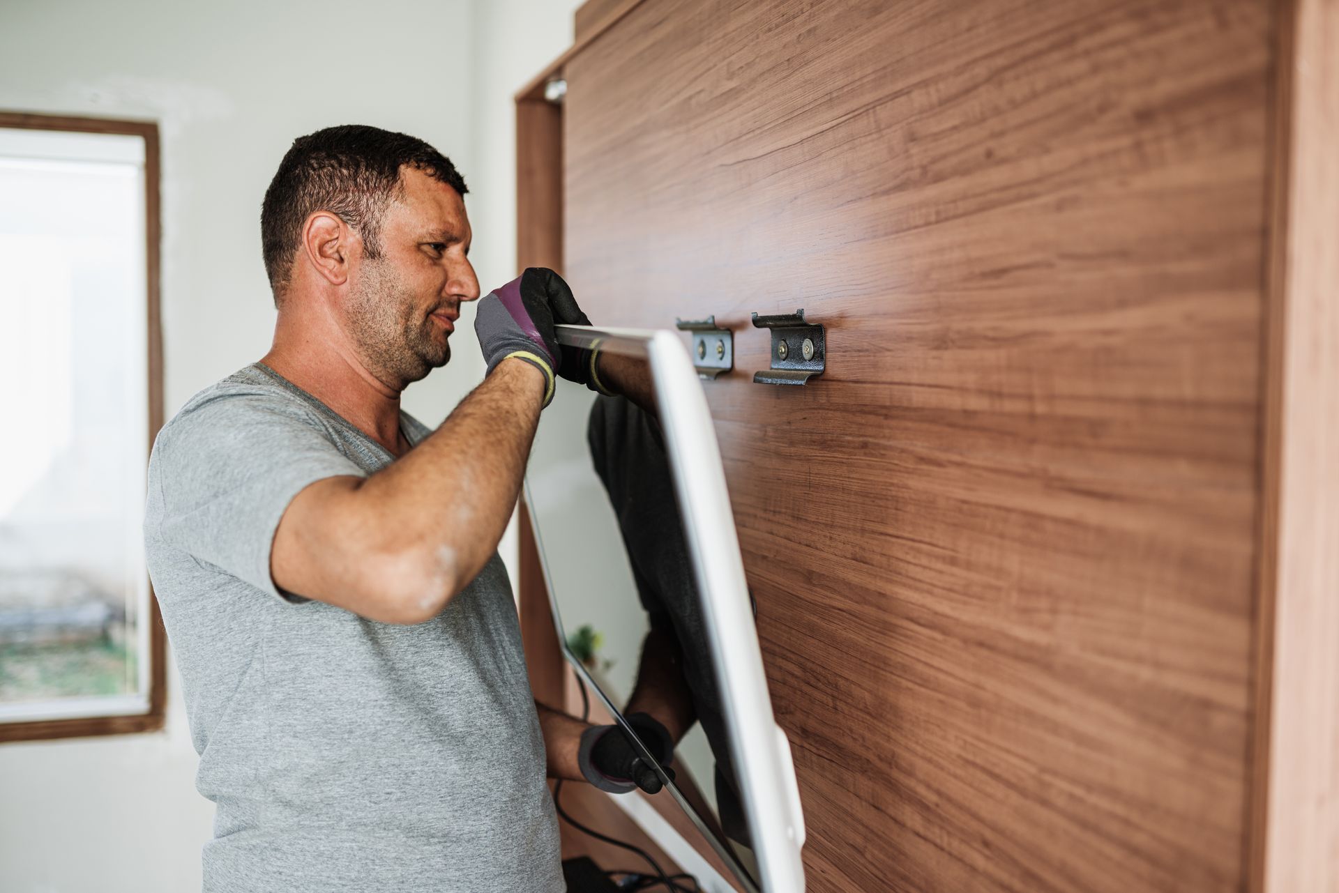 Man wearing gloves attaching a TV to a wooden wall. Man wearing gloves attaching a TV to a wooden wall.